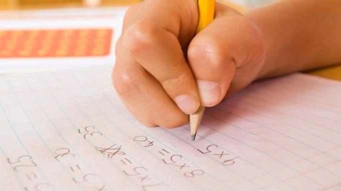Vaiko ranka, atliekanti namų užduotį, atliekant matematikos užduotis